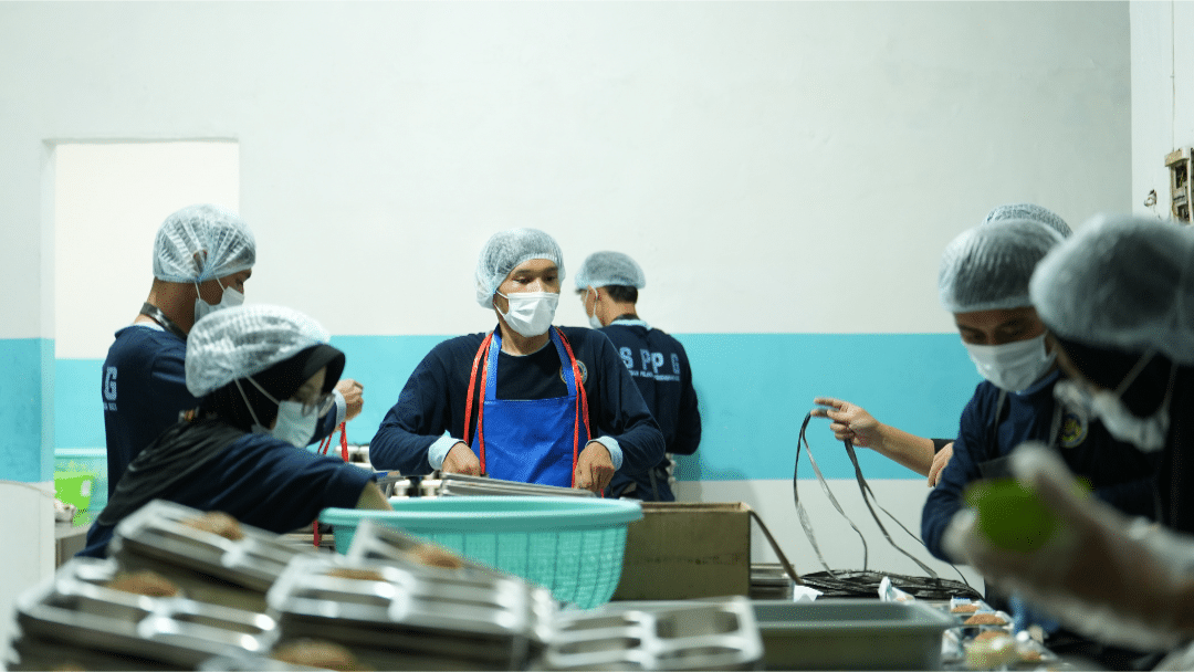 Petugas SPPG berseragam lengkap (masker, penutup kepala, sarung tangan) sedang menyiapkan menu makanan bergizi seimbang di dapur pelayanan yang higienis, sesuai audit Badan Gizi Nasional. (Sumber: BGN)