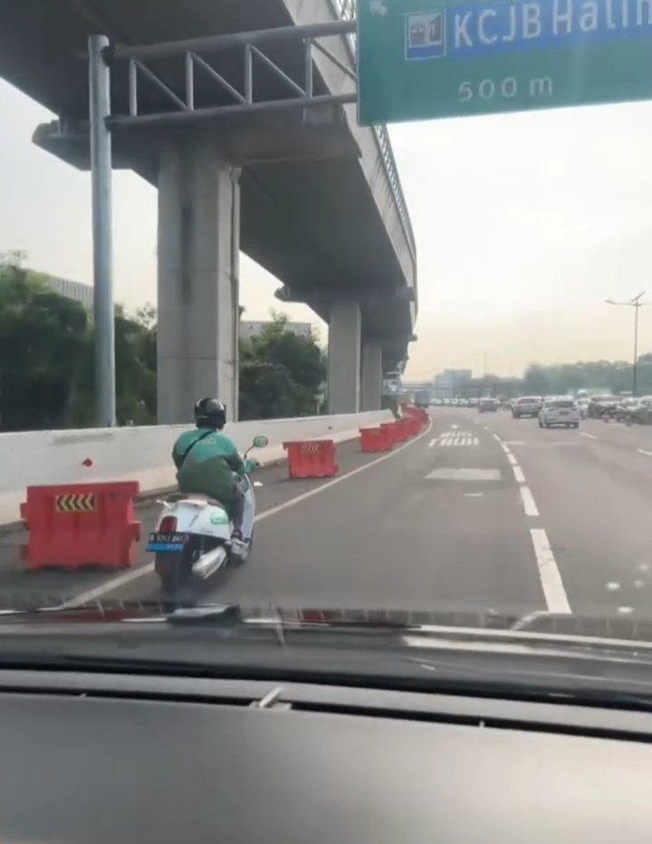 Sebuah video viral memperlihatkan seorang driver ojol menggunakan motor listrik Grab Electric melaju di lajur kiri Jalan Tol Jakarta-Cikampek, tak jauh dari penunjuk arah KCJB Halim. (Tangkapan layar/Viral Media Sosial)